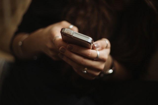 Ruke sa prstenovima drže mobilni telefon u providnoj futroli